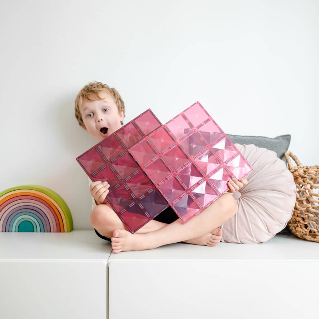 Child holding pink magnetic tile bases on a white surface