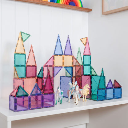 Colorful transparent magnetic building blocks on a white surface with a rainbow toy in the background.