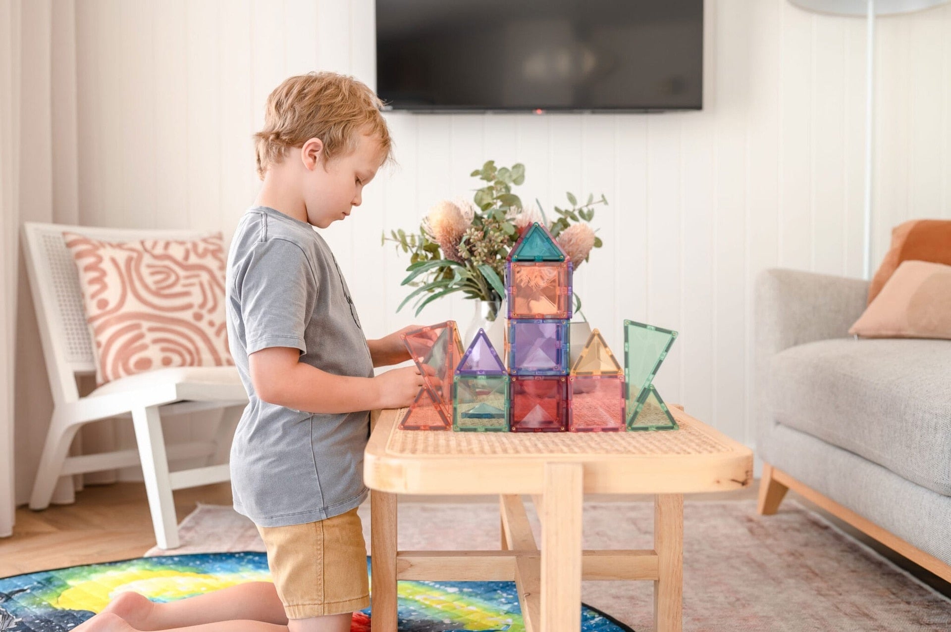 Child playing with colorful magnetic building blocks on a wooden table in a living room.