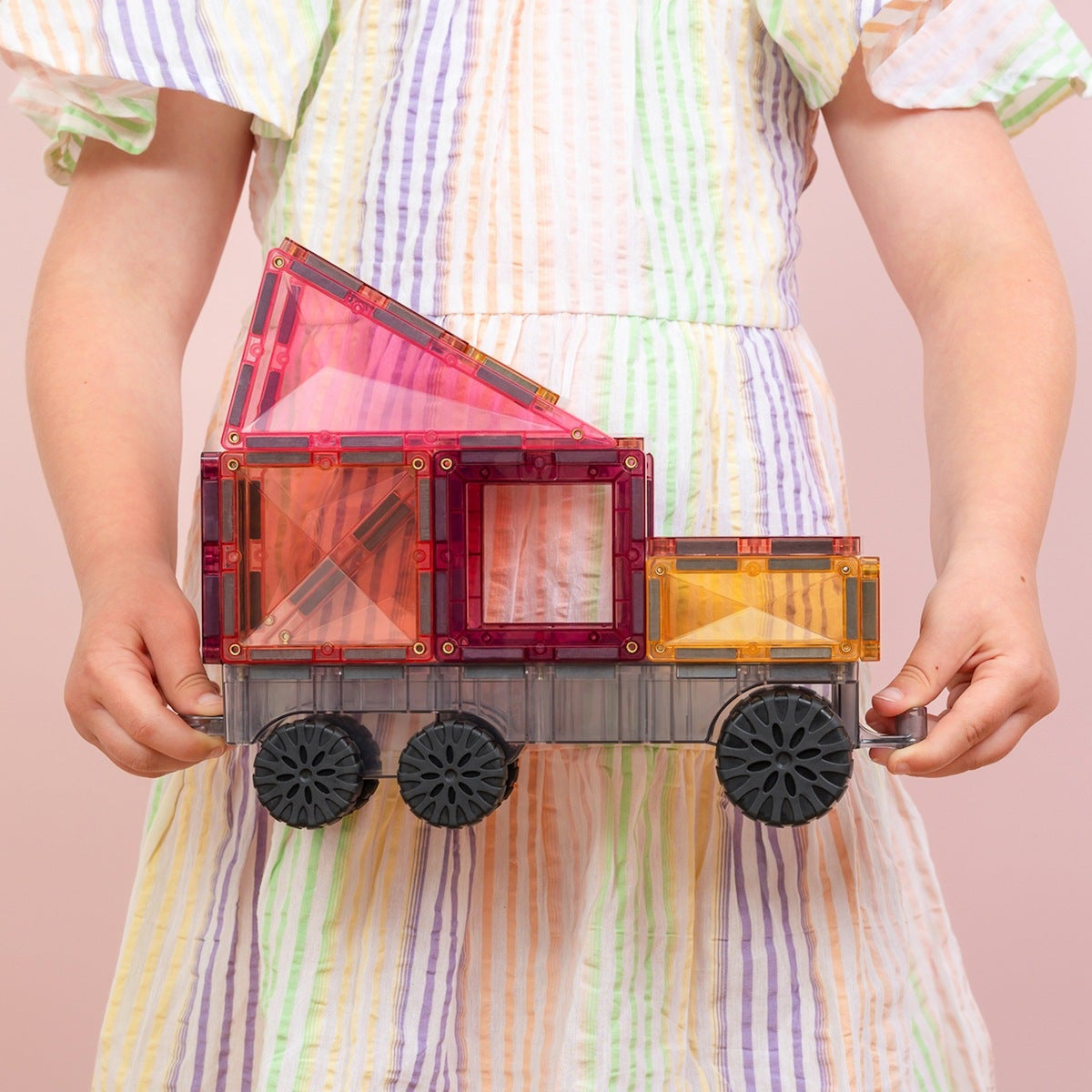 Child holding a colorful toy truck against a pink background