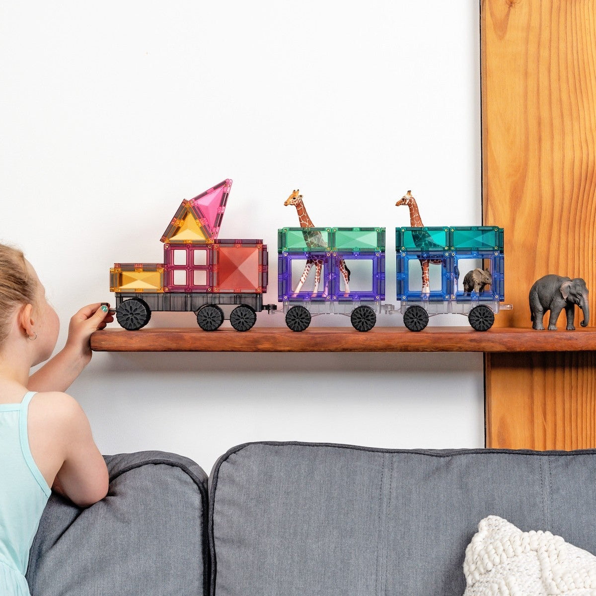 Child playing with a colorful toy train set on a shelf.