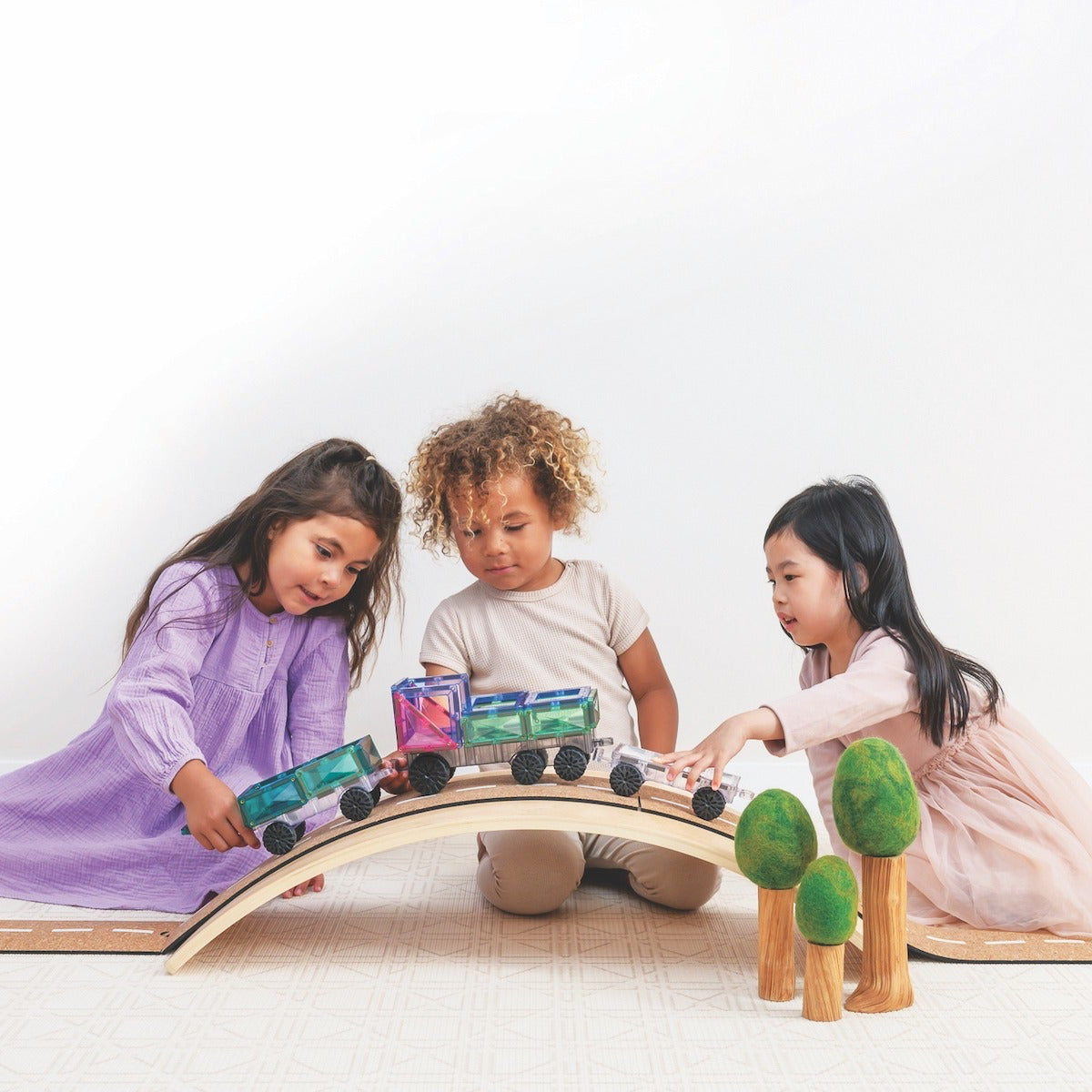Three children playing with a wooden train set on a white background