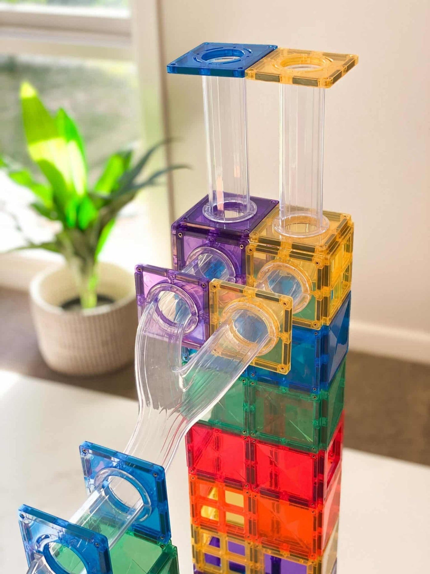 Colorful transparent building blocks stacked on a surface with a plant in the background
