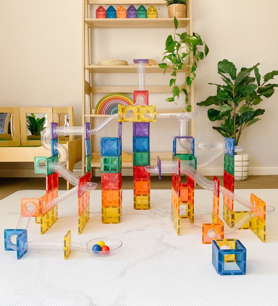 Colorful magnetic building blocks on a white surface with a shelf and plants in the background