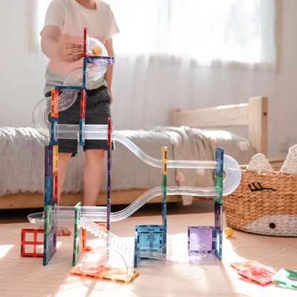 Child playing with a marble run toy set on a wooden floor.
