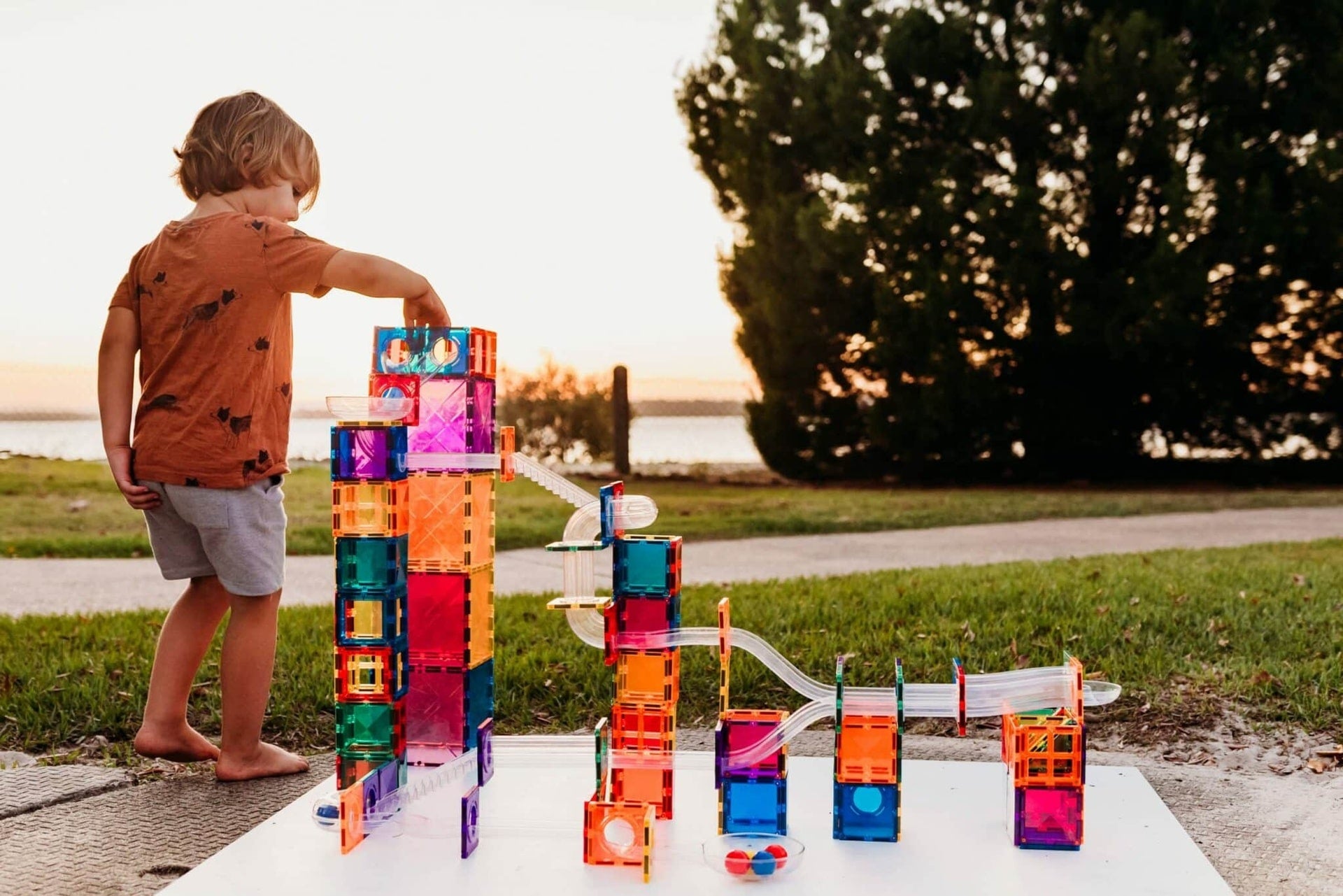 Child playing with colorful building blocks outdoors near a body of water.