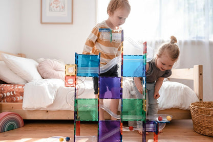 Two children playing with colorful building blocks in a bedroom.