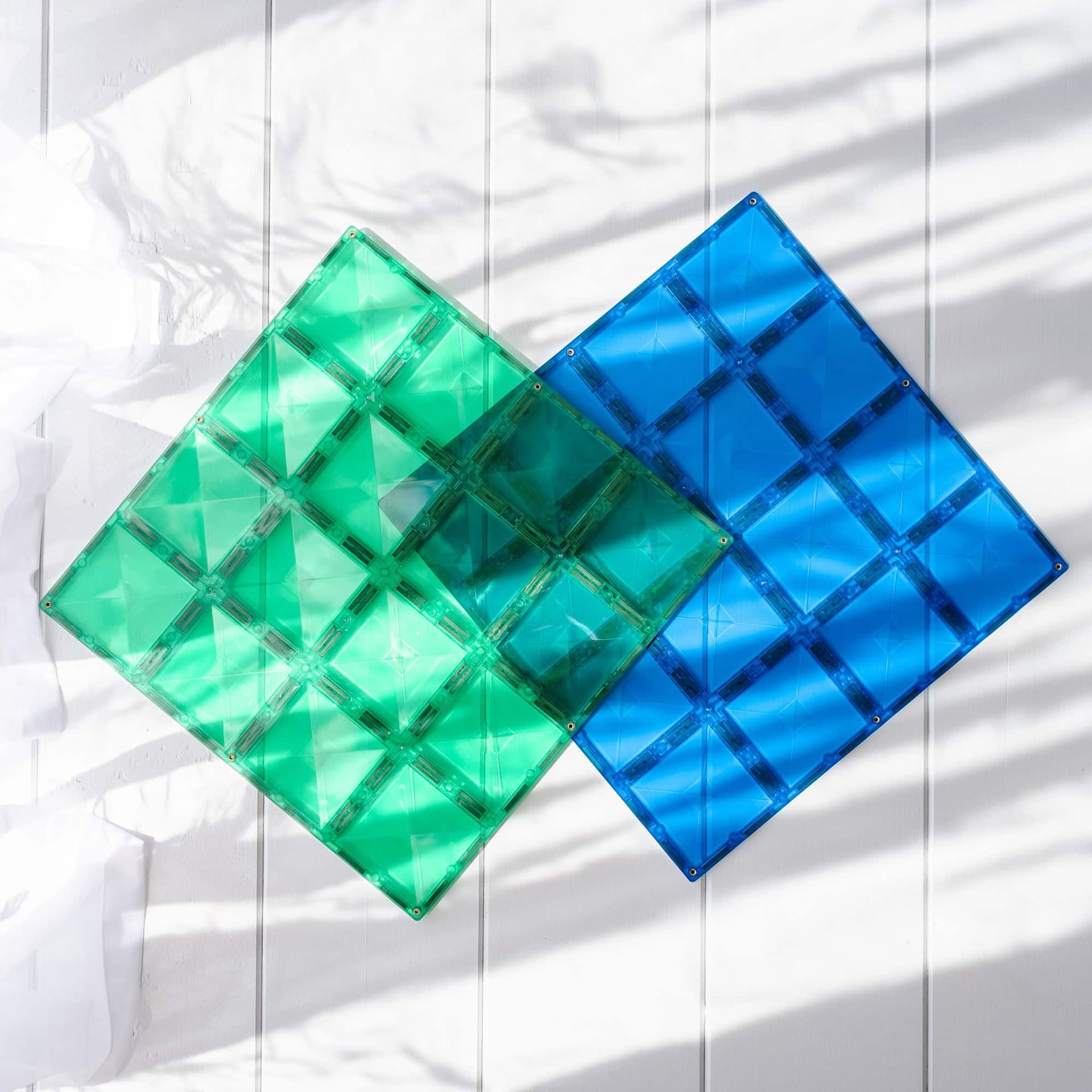 Two green and blue square magnetic base plates on a white background