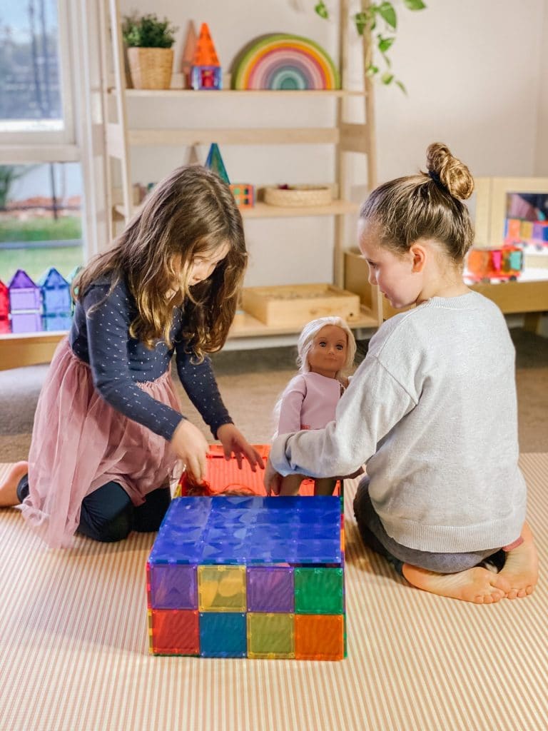 Two children playing with colorful magnetic tiles and a doll in a classroom setting
