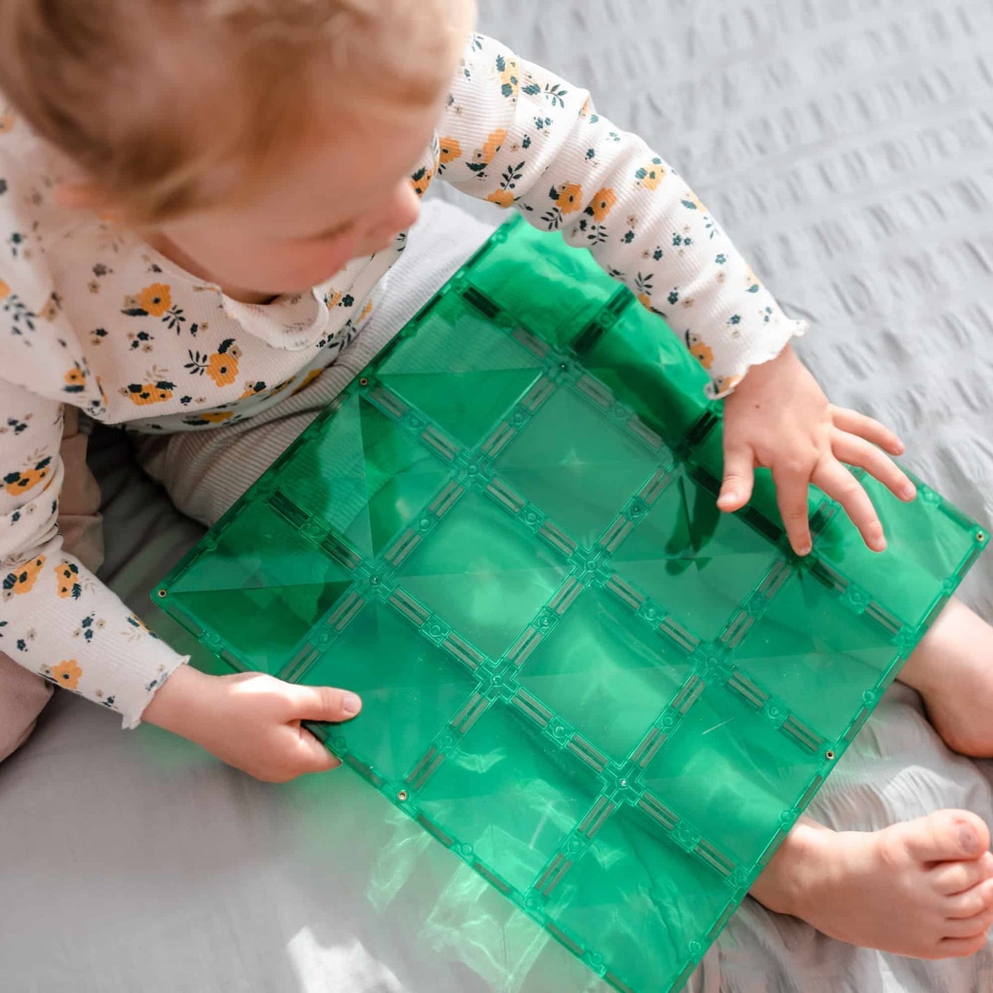 Child playing with a green transparent base plate on a gray surface