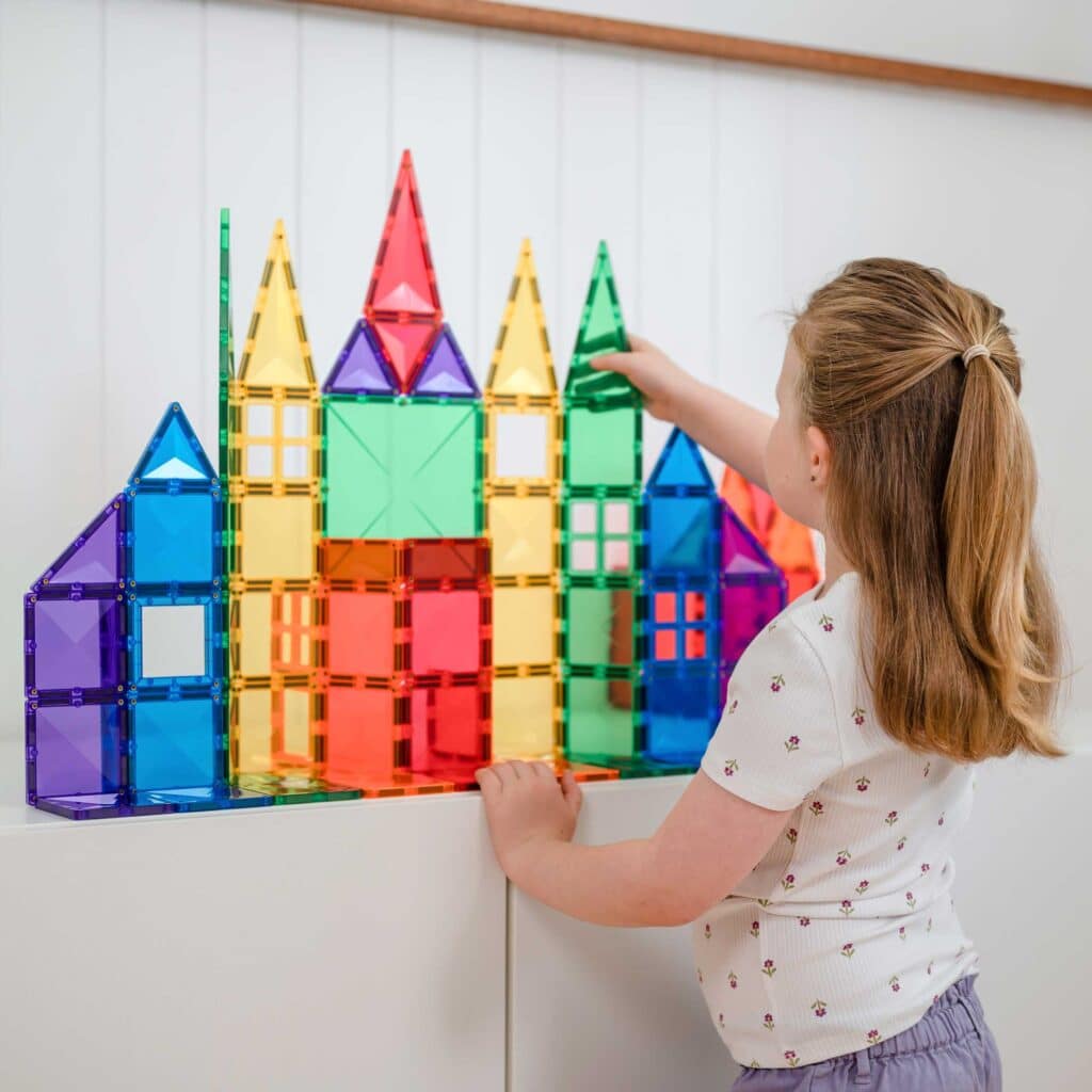 Child playing with colorful magnetic building blocks on a white wall
