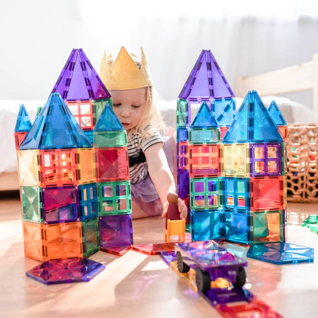 Child playing with colorful magnetic building blocks on a light surface.