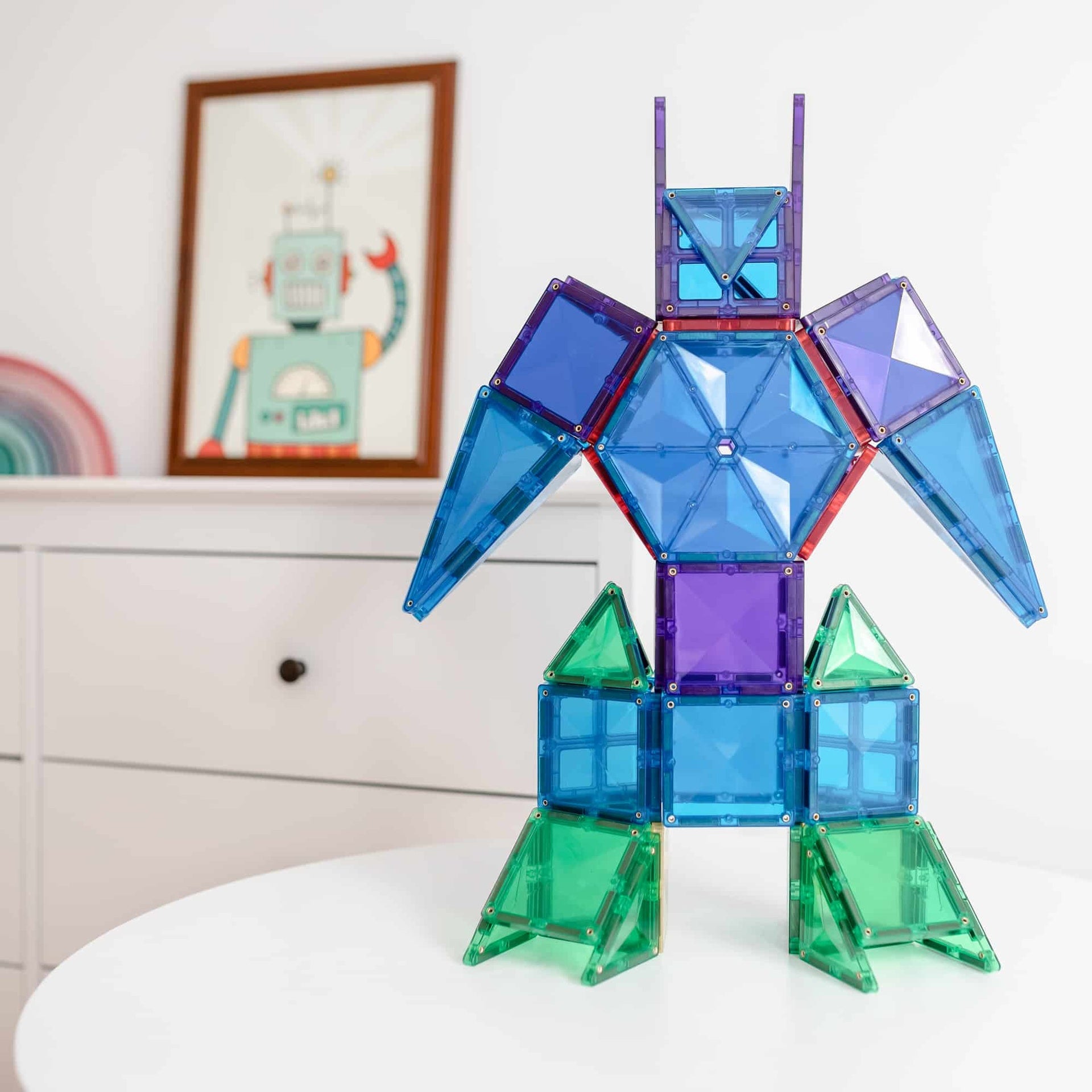 Colorful geometric robot model made of interlocking pieces on a white surface with a framed picture in the background.