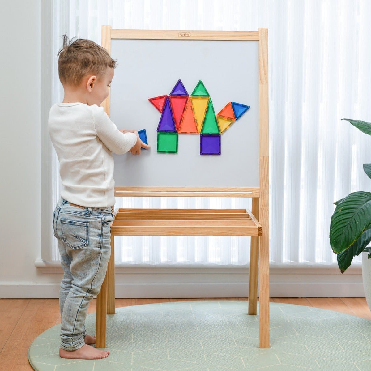 Child playing with colorful magnetic shapes on a wooden easel.