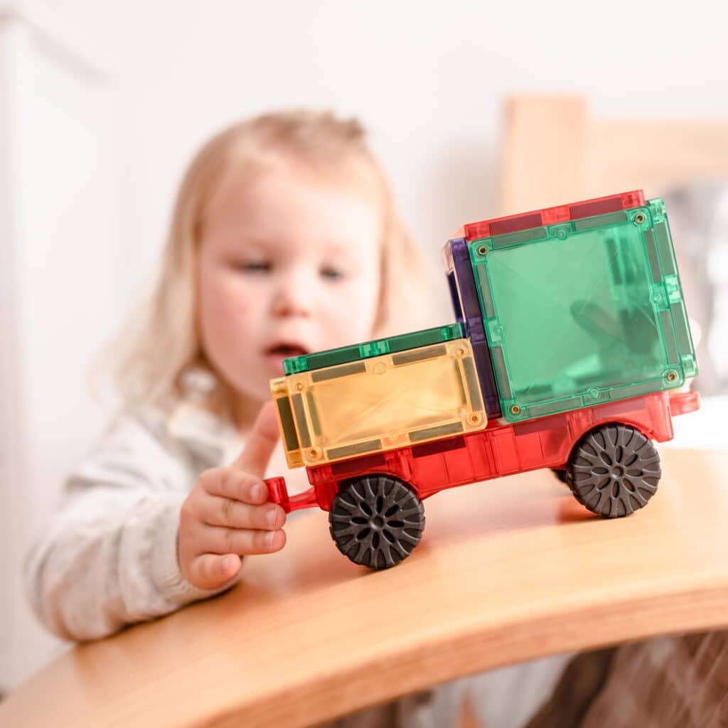 Child playing with a colorful toy truck on a wooden surface