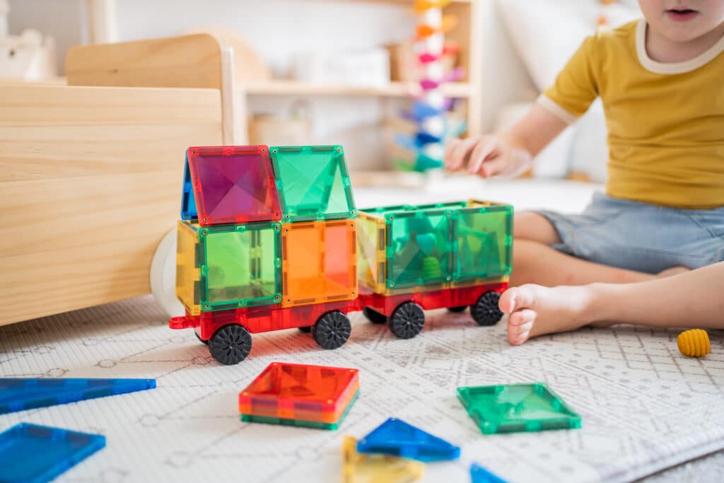 Child playing with colorful magnetic building blocks on a carpeted floor.