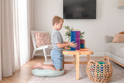 Child playing with colorful blocks on a wooden table in a living room.