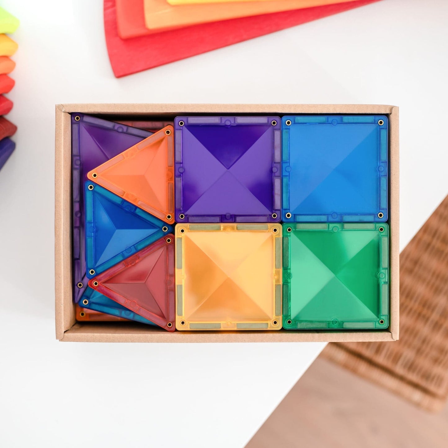 Colorful geometric magnetic building blocks in a wooden box on a white surface.