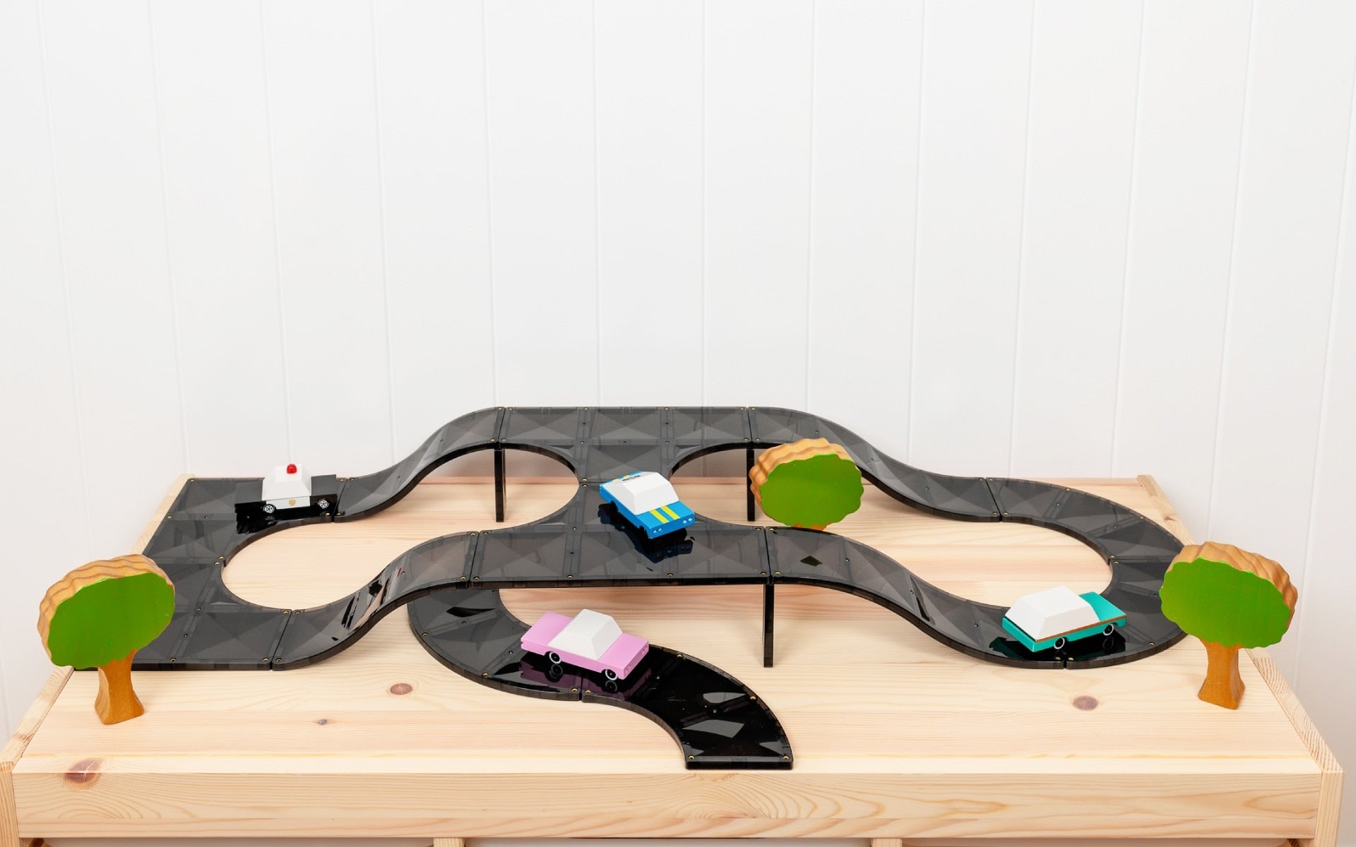Toy race track set with cars and trees on a wooden base against a white background