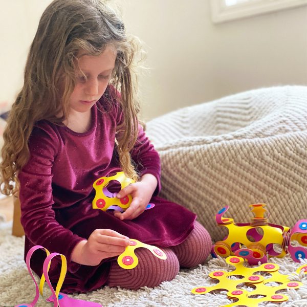 Child playing with colorful toy gears on a carpeted floor.