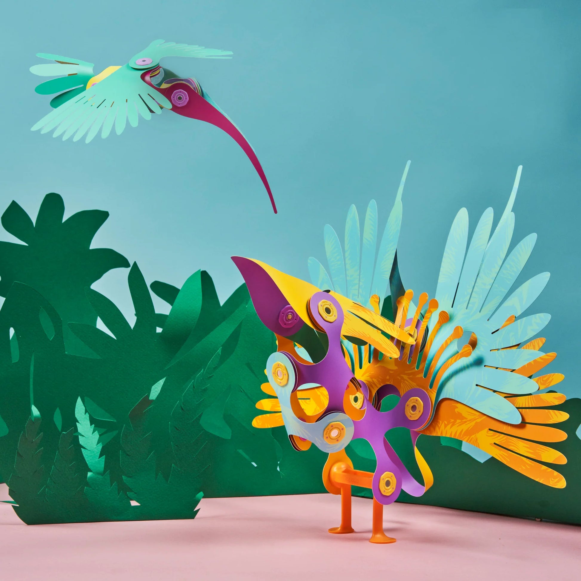 Colorful paper sculpture of a bird with another bird flying above on a teal background.