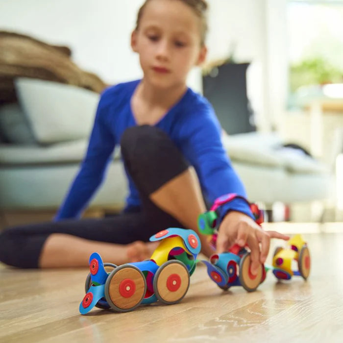 Child playing with colourful toy cars on a wooden floor.