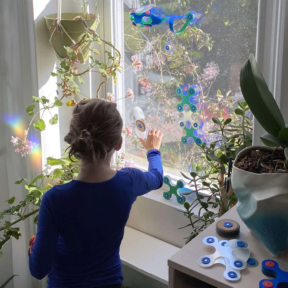 Person decorating a window with colorful fidget spinners and plant decorations.