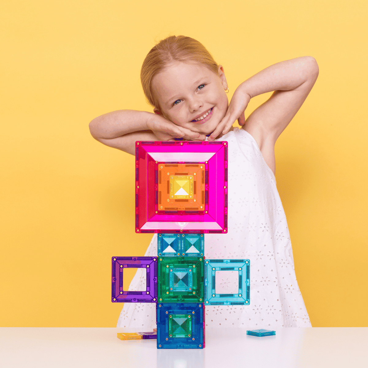 Child playing with colorful magnetic building blocks against a yellow background