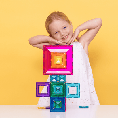 Child playing with colorful magnetic building blocks against a yellow background