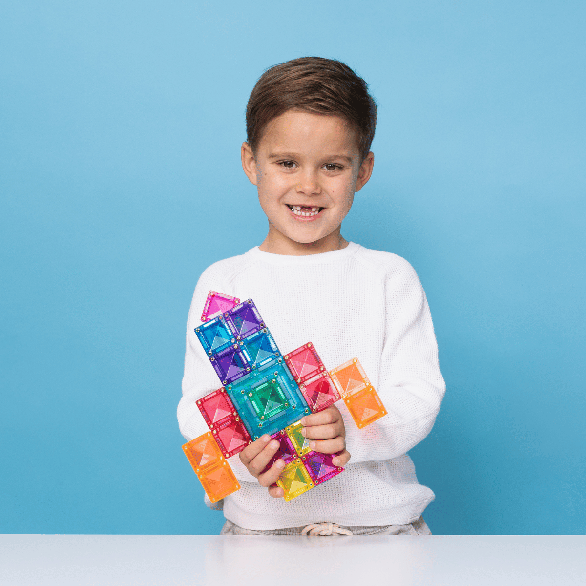 Child holding colorful magnetic building blocks against a blue background
