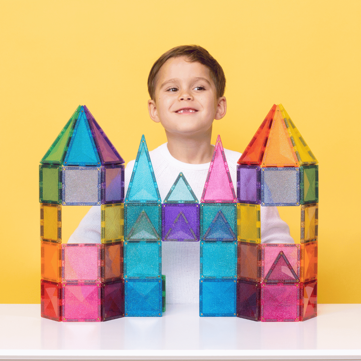 Child with a colorful magnetic building block castle against a yellow background