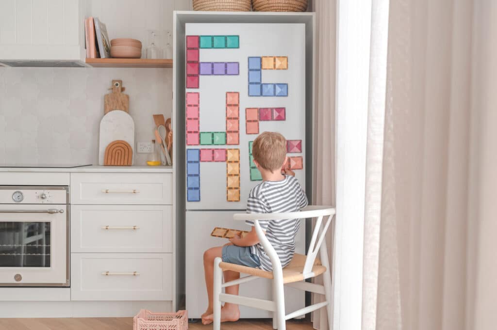 Child playing with colorful magnetic blocks on a refrigerator door in a kitchen.