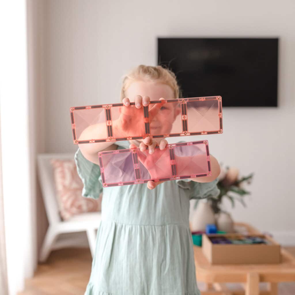 Child holding a transparent pink organizer with compartments in a living room.