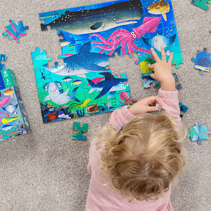 Child playing with an underwater-themed puzzle on a carpeted floor