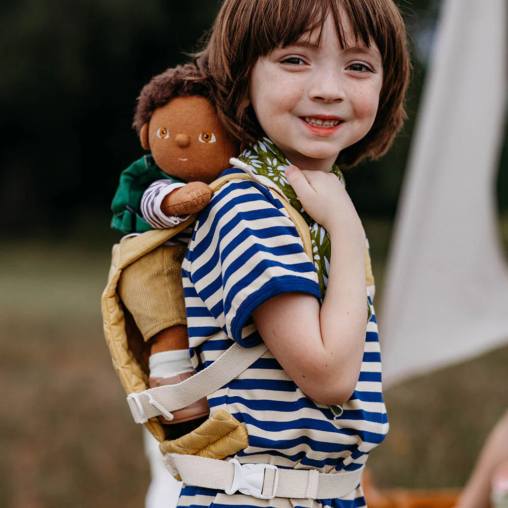 Child holding a doll in a backpack with a blurred outdoor background