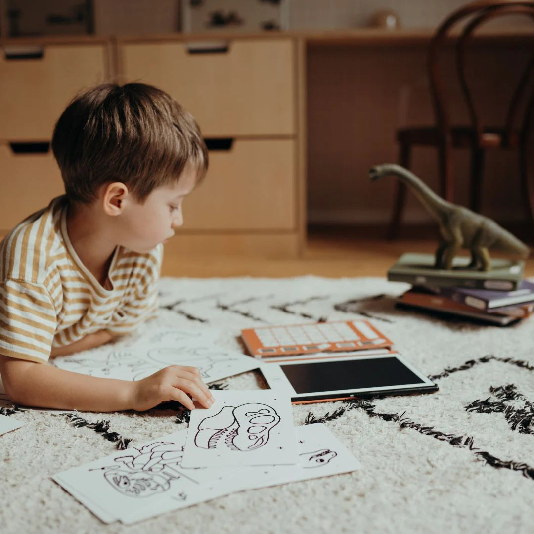 Child sitting on a rug with coloring books and a tablet in a home setting