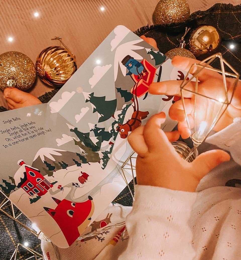 Person holding a Christmas-themed card with festive decorations and lights in the background.