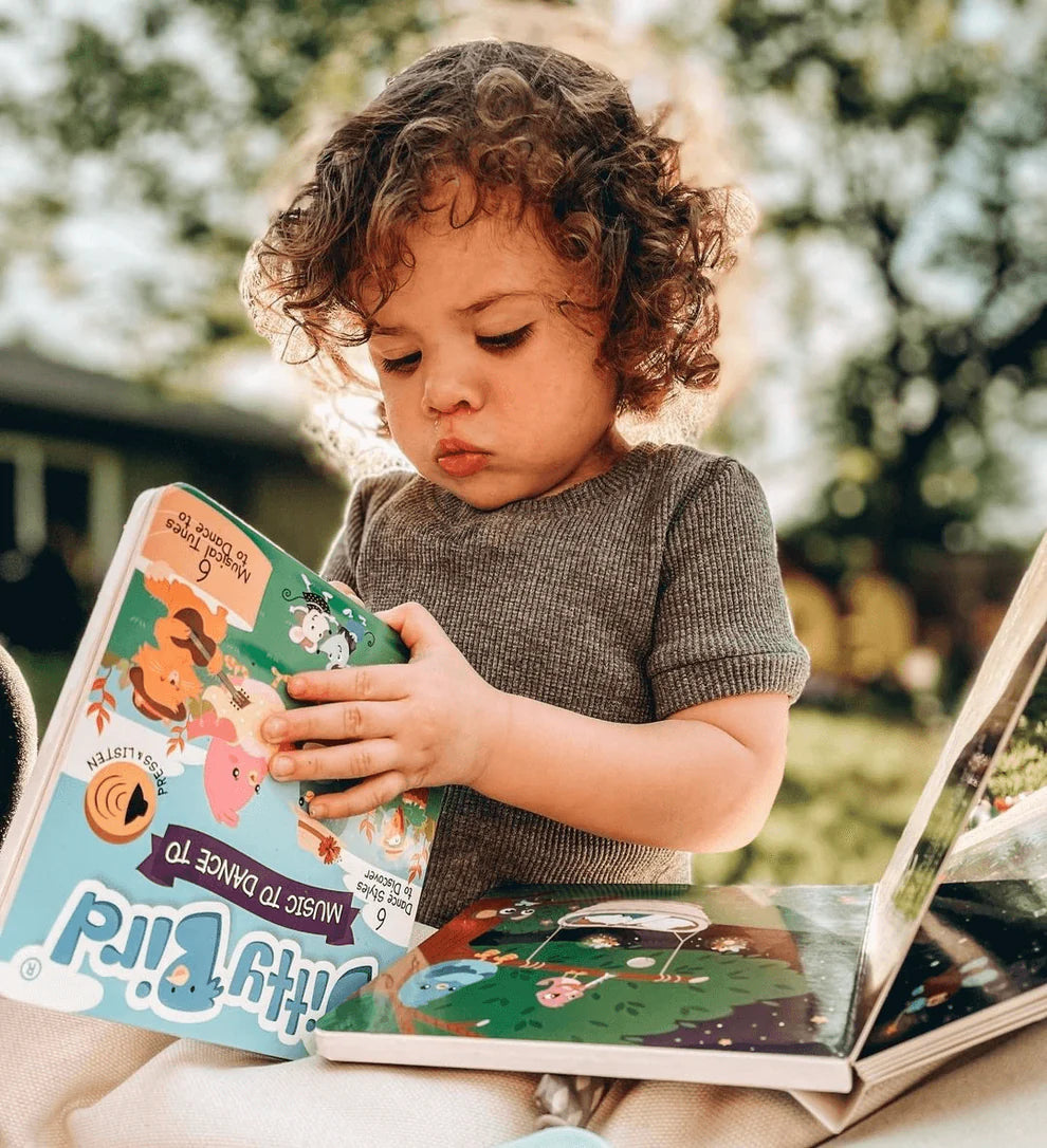 Child reading a book outdoors with trees in the background