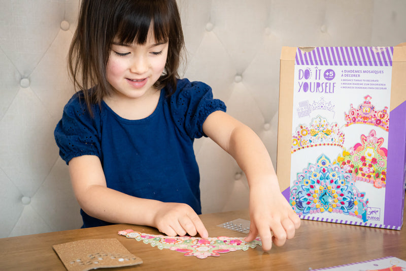 Child putting stickers on a paper tiara at a table. Do It Yourself packaging on the table.