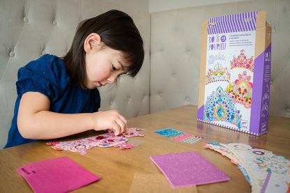 Child putting stickers on a paper tiara at a table. Do It Yourself packaging on the table.