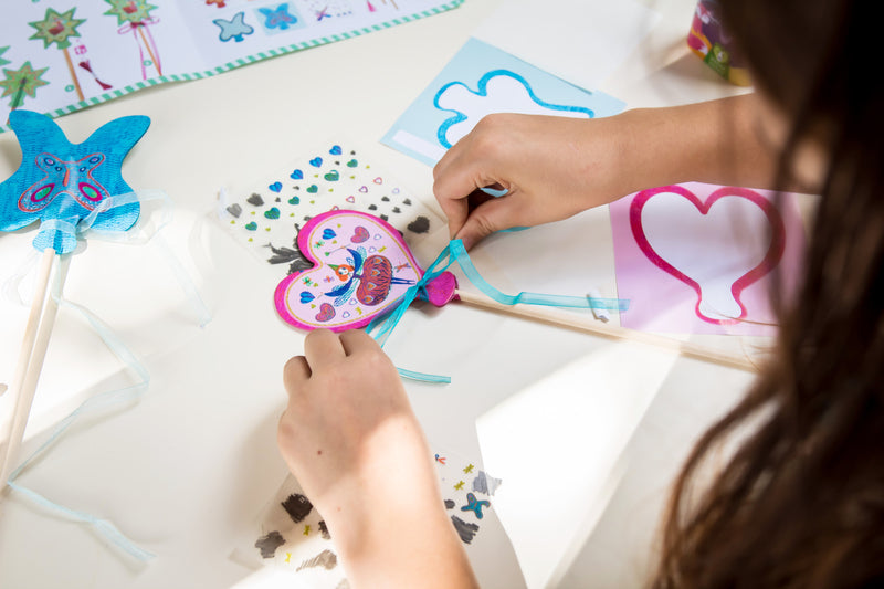 Child tying blue string on wand with pink fairy at a table.