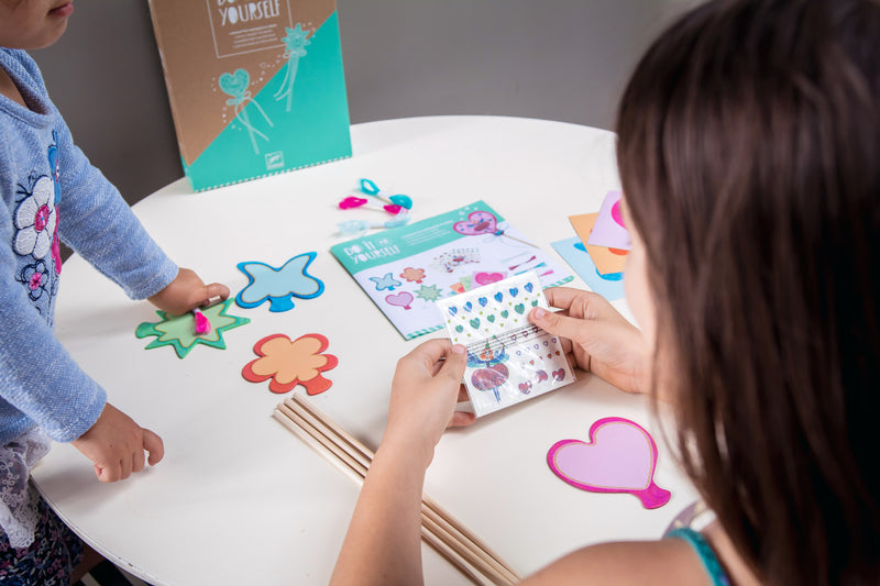 Child holding sticks and pencil at a table. 