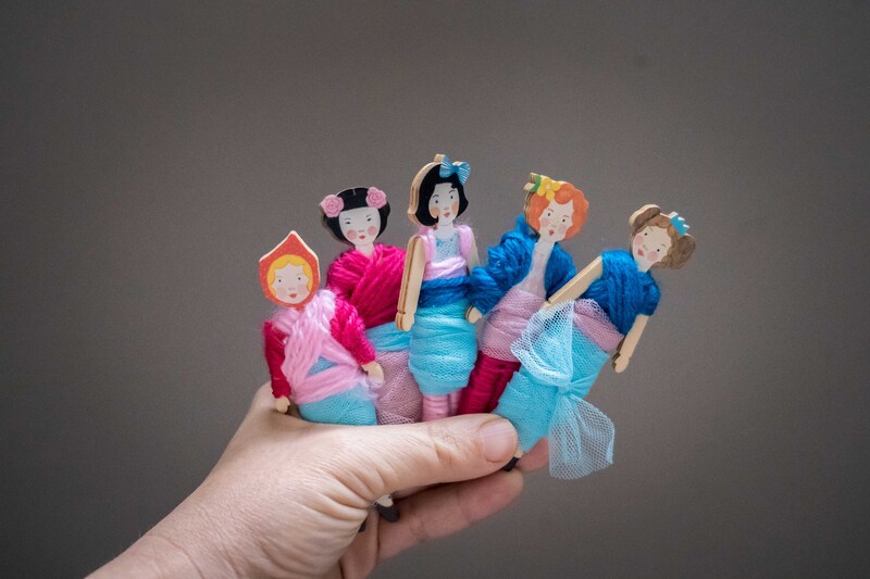 Hand holding five wooden dolls on grey background.