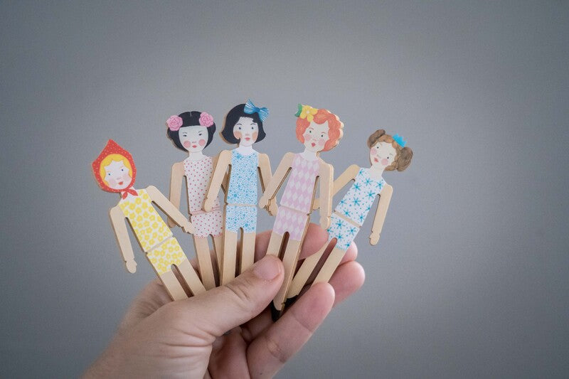 Hand holding five wooden dolls on grey background.