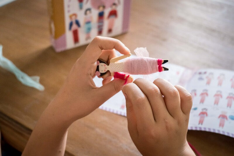 Child wrapping tulle around doll with instructions and packaging on table.