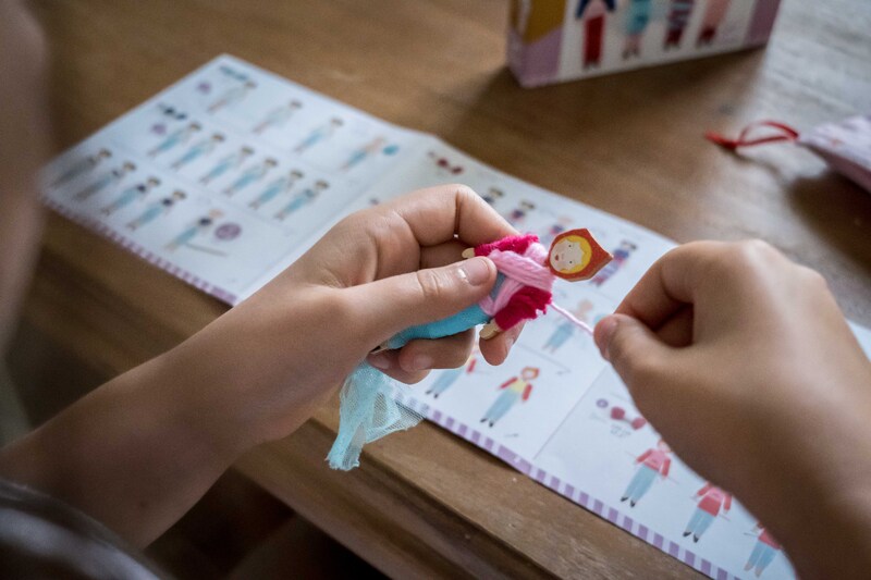 Child wrapping wool around doll with instructions and packaging on table. 