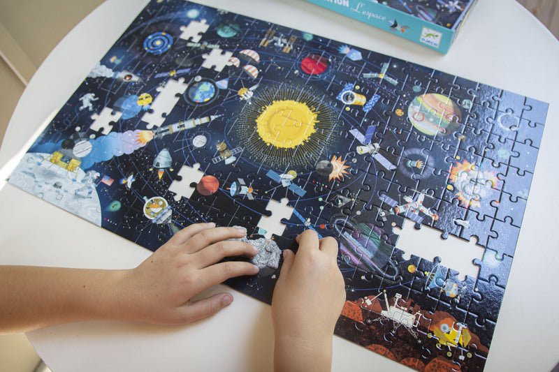 Children's hands working on a solar system-themed puzzle on a white table.