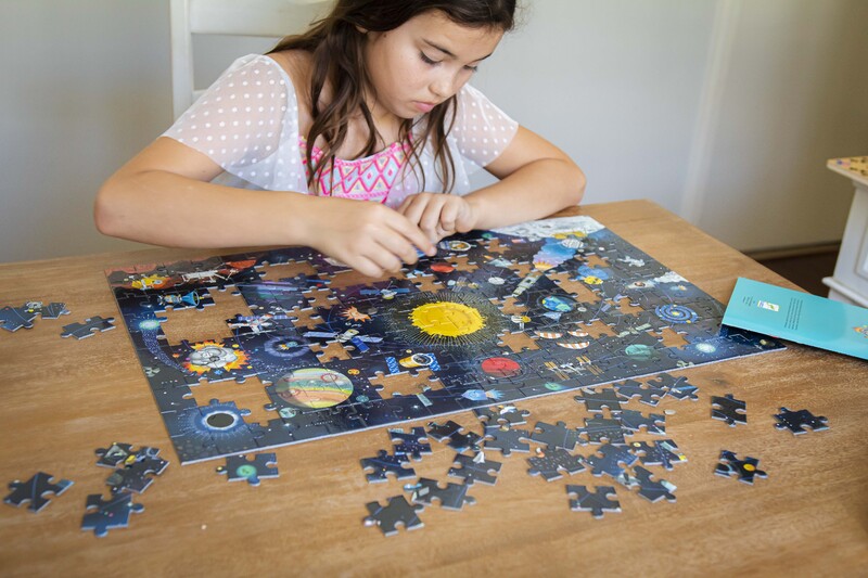 Girl working on a puzzle with space-themed pieces on a wooden table.