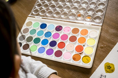 Open watercolor palette with various colors on a wooden surface