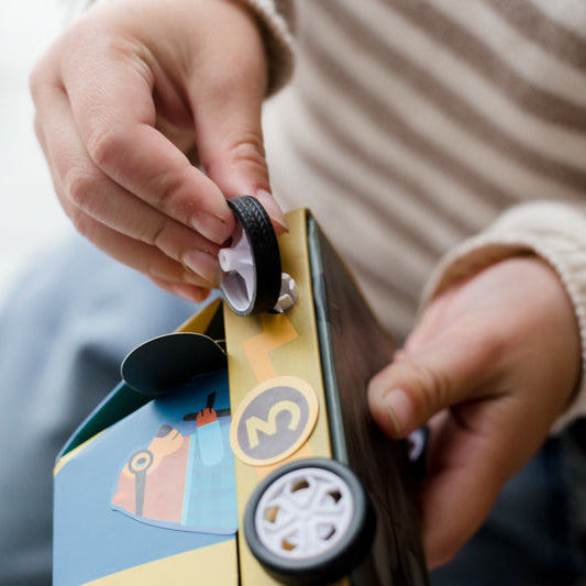 Close-up of a hand holding a toy box with wheels, blurred background